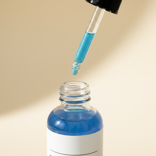 Dropper with light blue copper peptide serum above the open bottle