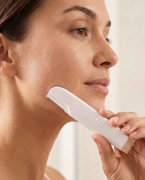 Woman gliding the GlowPrep dermaplaning device along her cheek to remove peach fuzz